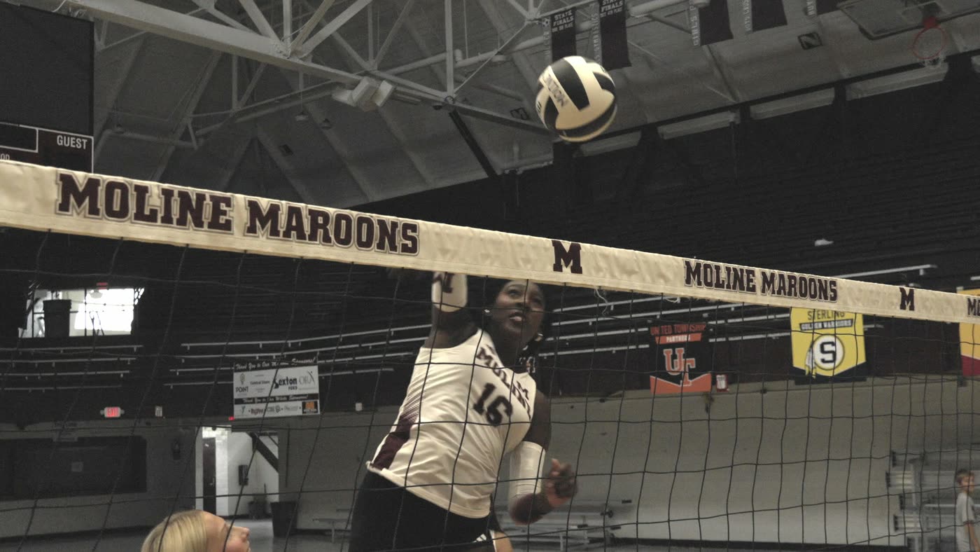 Volleyball player attacking at the net under the Moline Maroons banner at Wharton Field House