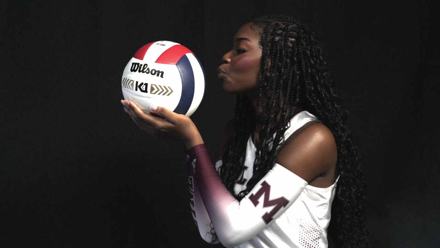 Volleyball player holding a ball at eye level against a black media-day background