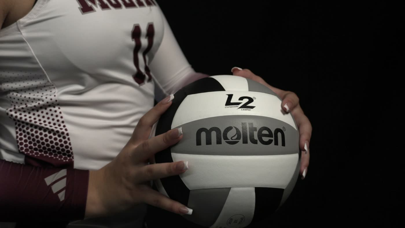 Close detail of a player’s hands and jersey gripping a game volleyball